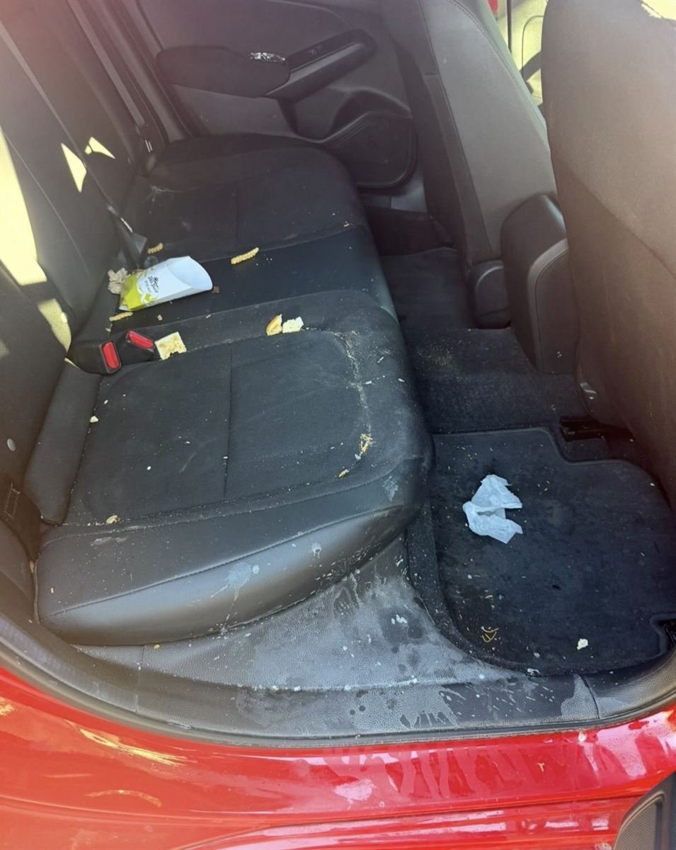 Same black rear car seats before, covered in food crumbs and trash